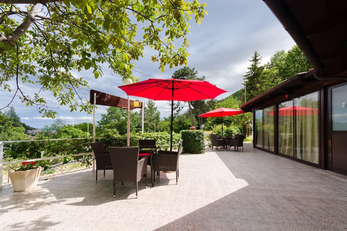 Eine Außenpatio mit Tischen und Stühlen, roten Sonnenschirmen und Blick auf die umliegende Landschaft.