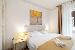 Habitación de hotel con cama, mesita de noche, lámpara, un cuadro y ventana con cortinas.