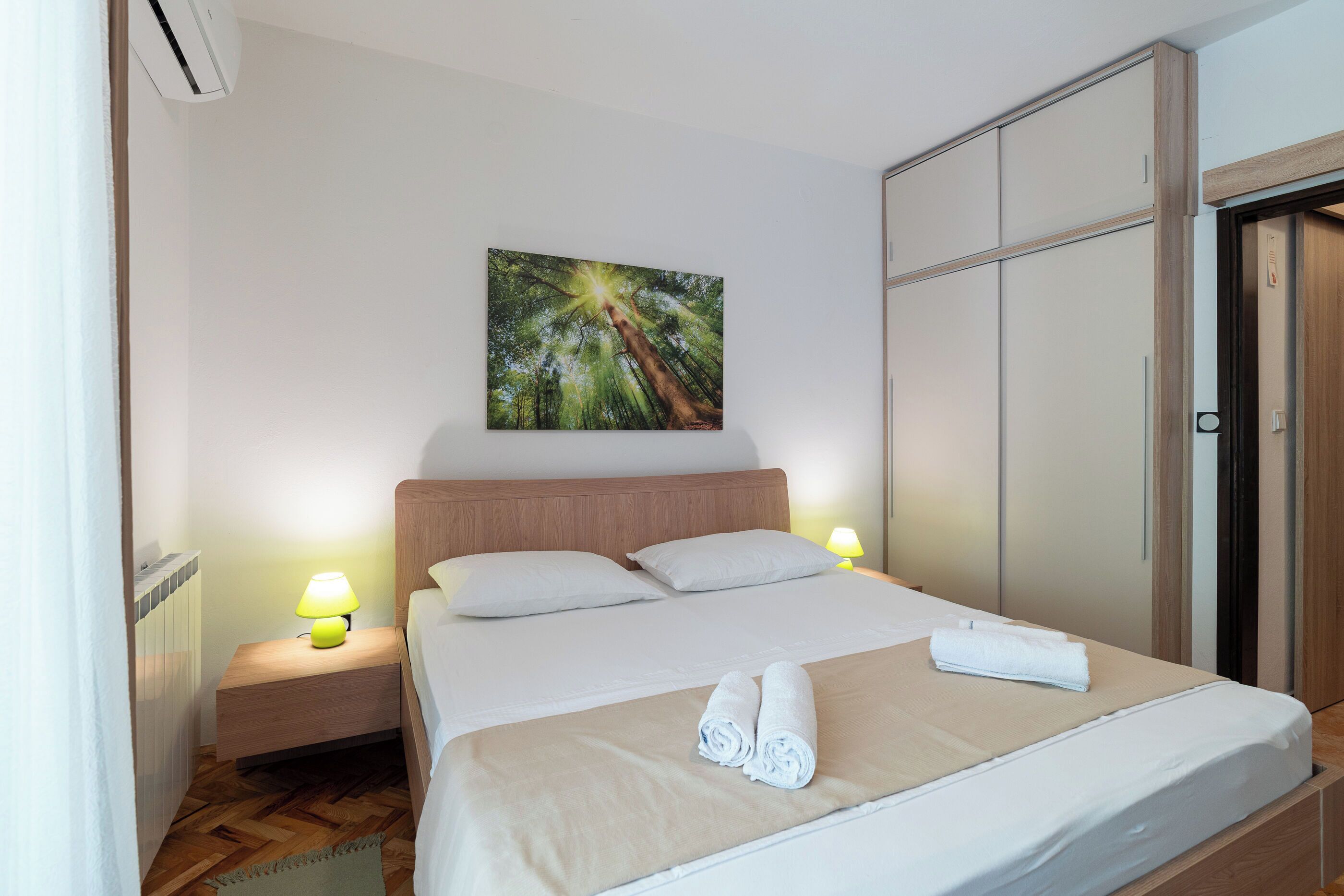 Una habitación de hotel con una cama, dos lámparas de noche, un cuadro en la pared y un armario.