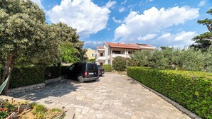 A paved driveway leading to a house with a red-tiled roof, surrounded by greenery and a parked car. - Apartments Ivo (Pag)