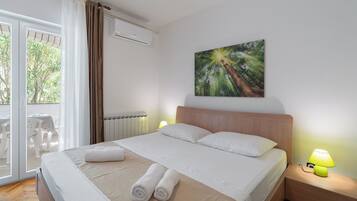 Ein Hotelzimmer mit einem Bett, einem Gemälde, einem Fenster mit Vorhängen, einer Heizung und einem Tisch mit Stühlen davor.