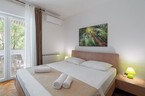 Habitación de hotel con cama, un cuadro, ventana con cortinas, radiador y una mesa con sillas afuera.