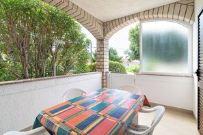 Un pequeño patio con mesa y sillas, un ventanal grande y vista a zonas verdes.