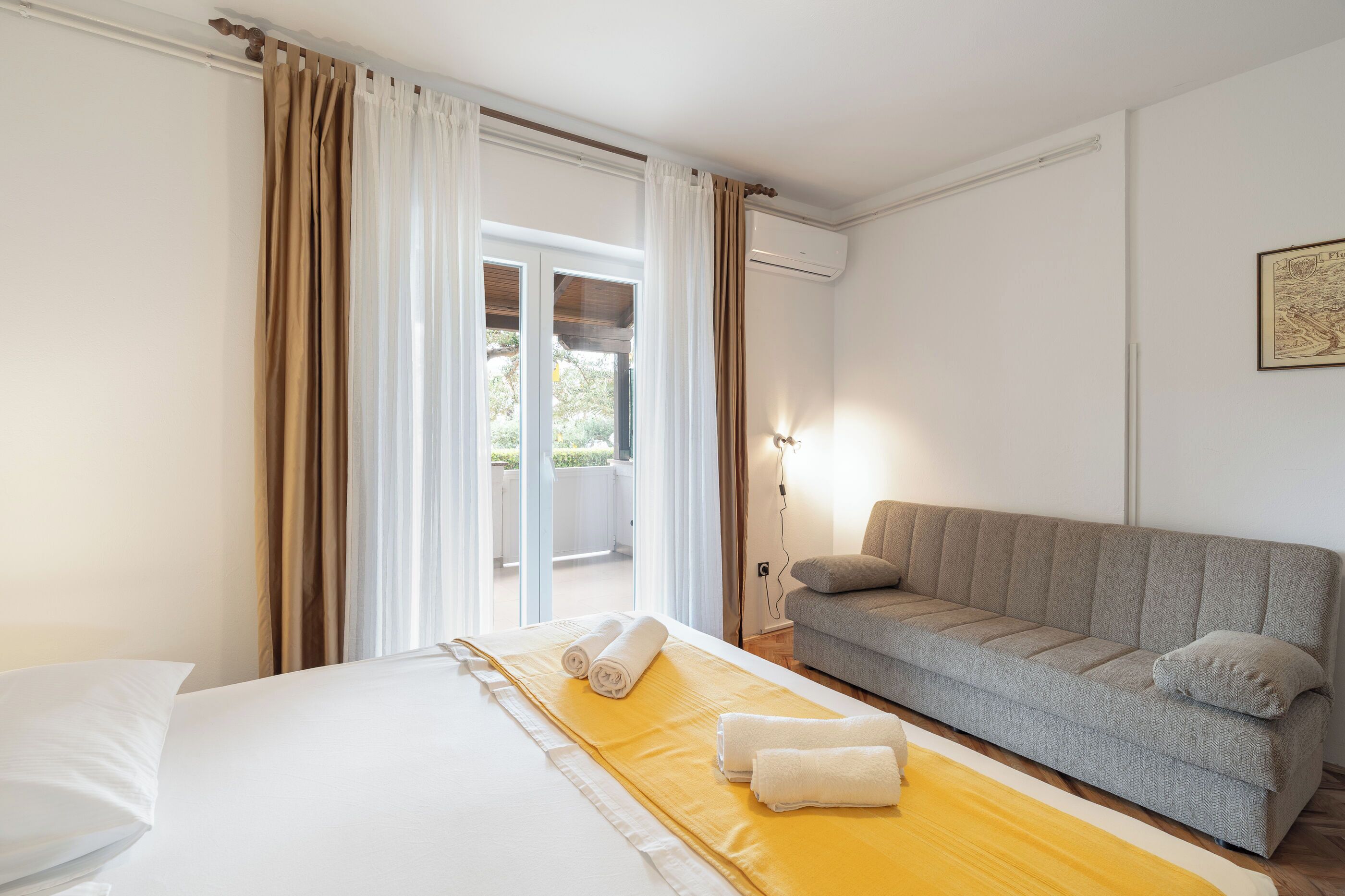 A hotel room with a bed, a sofa, a balcony, and an air conditioning unit.