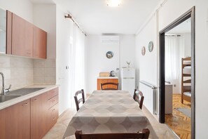 A compact kitchen with a sink, cabinets, and a dining area with a table and chairs. - Apartments Ivo (Pag)