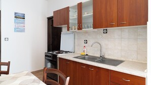 A kitchen with wooden cabinets, a stove, a sink, and a calendar on the wall. - Apartments Ivo (Pag)