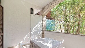 A balcony with a table and chairs, a view of trees, and a window with a curtain. - Apartments Ivo (Pag)