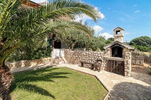 A stone-walled outdoor area with a stone bench and a small wooden structure, possibly a barbecue or grill. - Apartments Ivo (Pag)