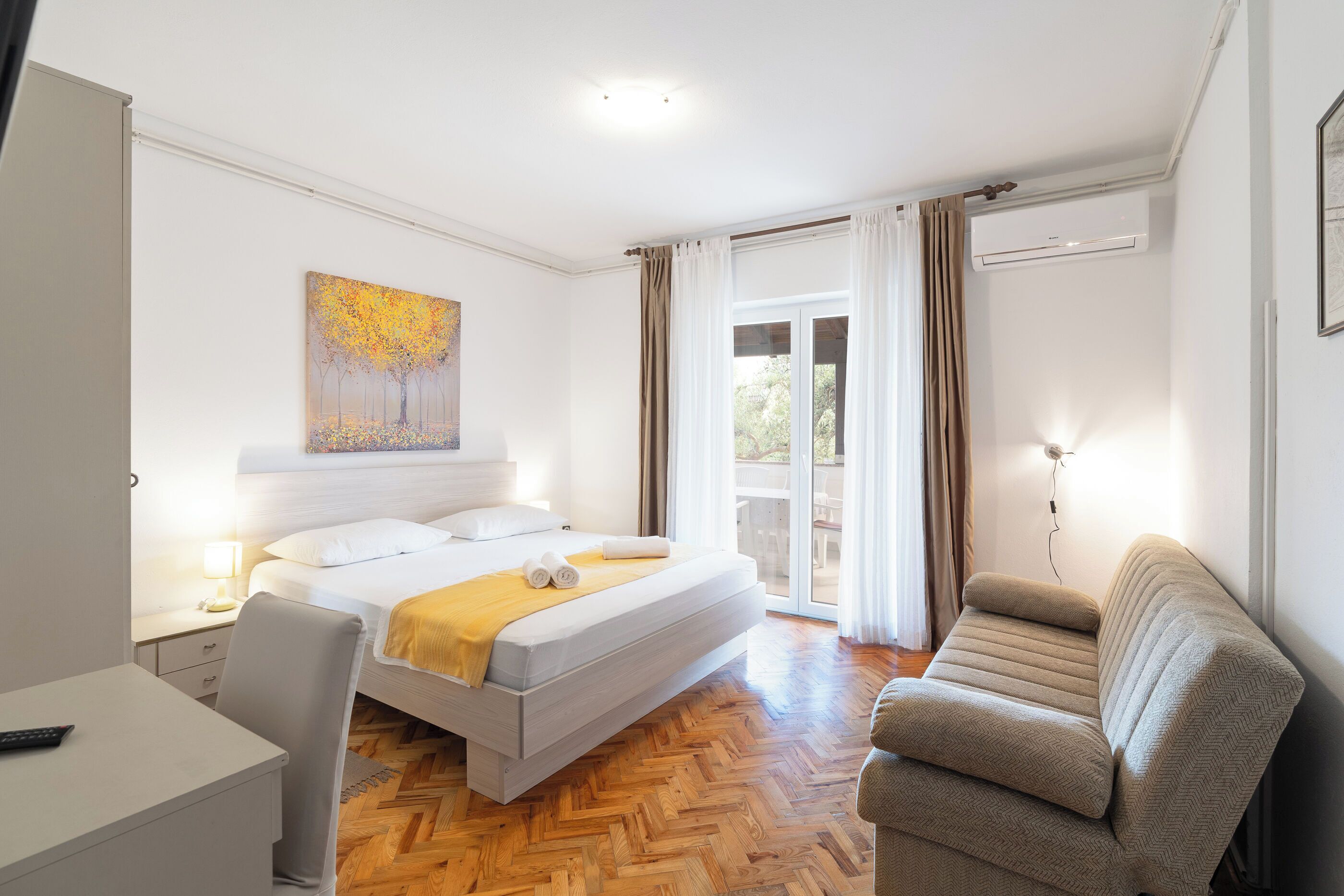 Habitación de hotel con cama, escritorio, una silla, un cuadro y vistas al exterior.