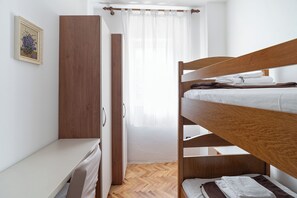 Una cama litera con cabecera de madera, una mesita de noche blanca y un armario.