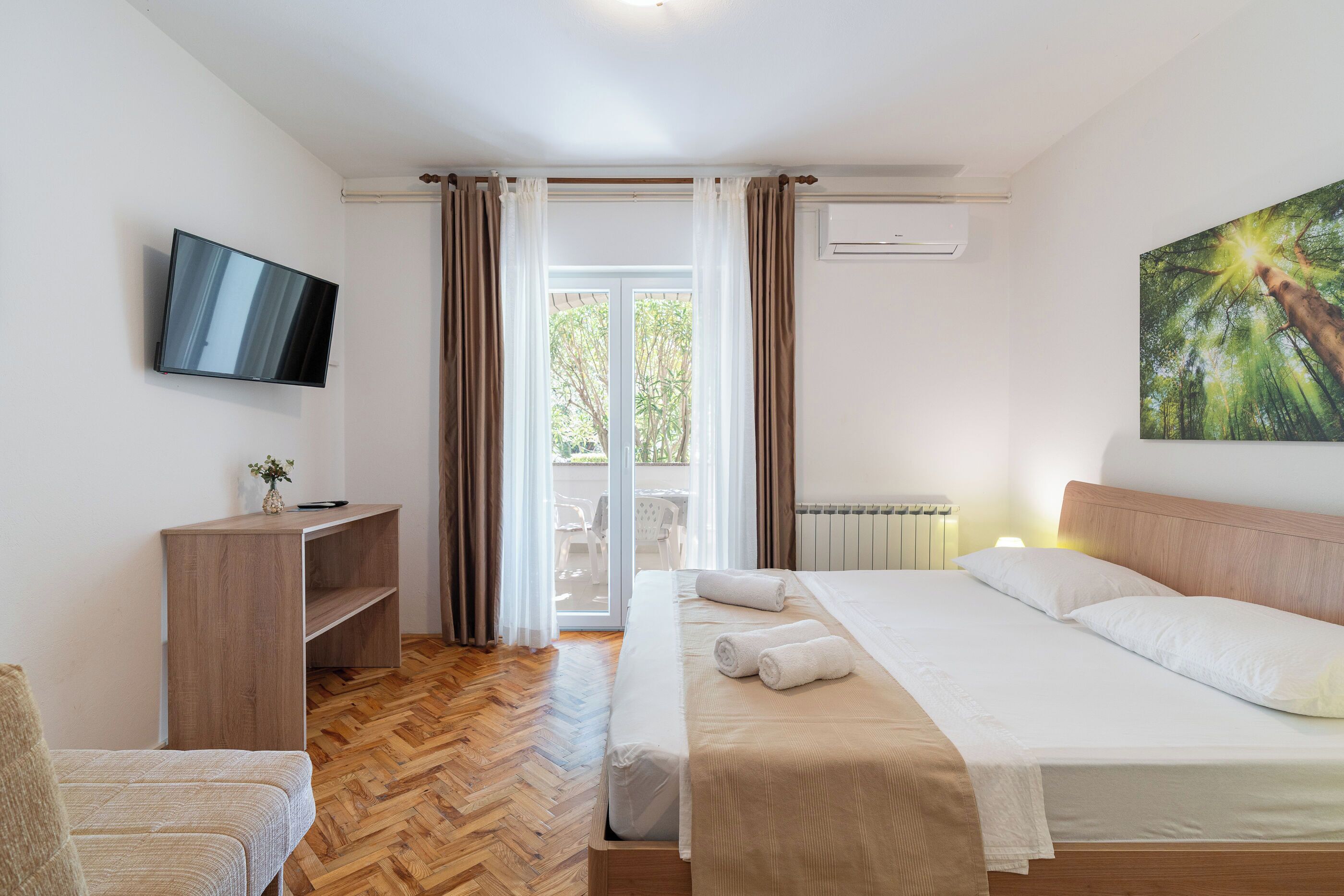 Hotellihuone, jossa on sänky, työpöytä, televisio ja taulu.