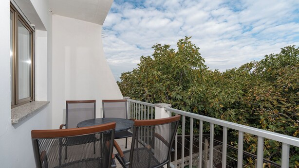 Ein Balkon mit Tisch und Stühlen, eine weiße Wand und Blick auf Bäume.