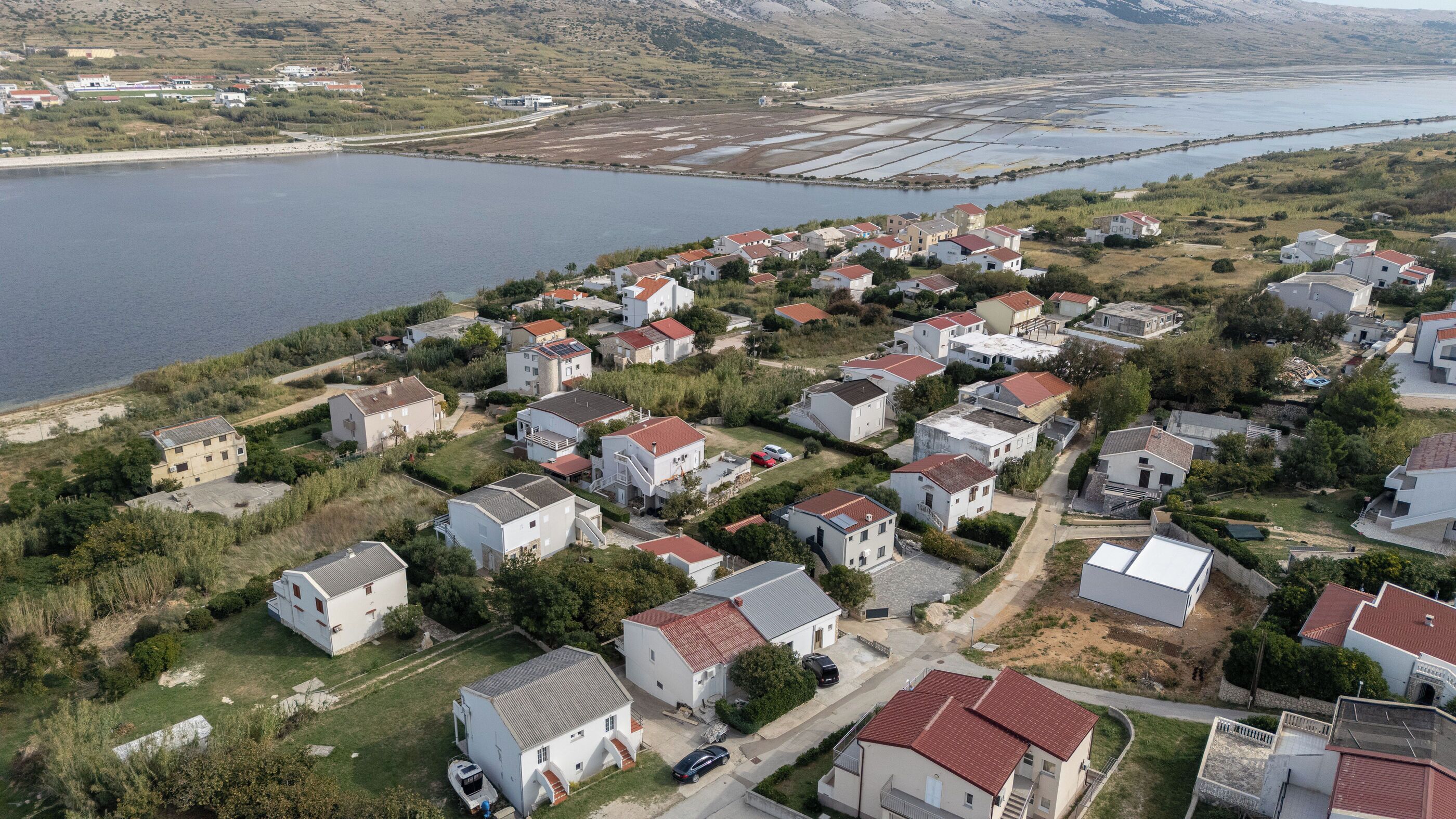 An aerial view of a residential area with houses, a lake, and a distant industrial area.