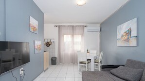 Ein Wohnzimmer mit Fernseher, grauem Sofa, weißem Tisch und Kunstwerken an den Wänden.