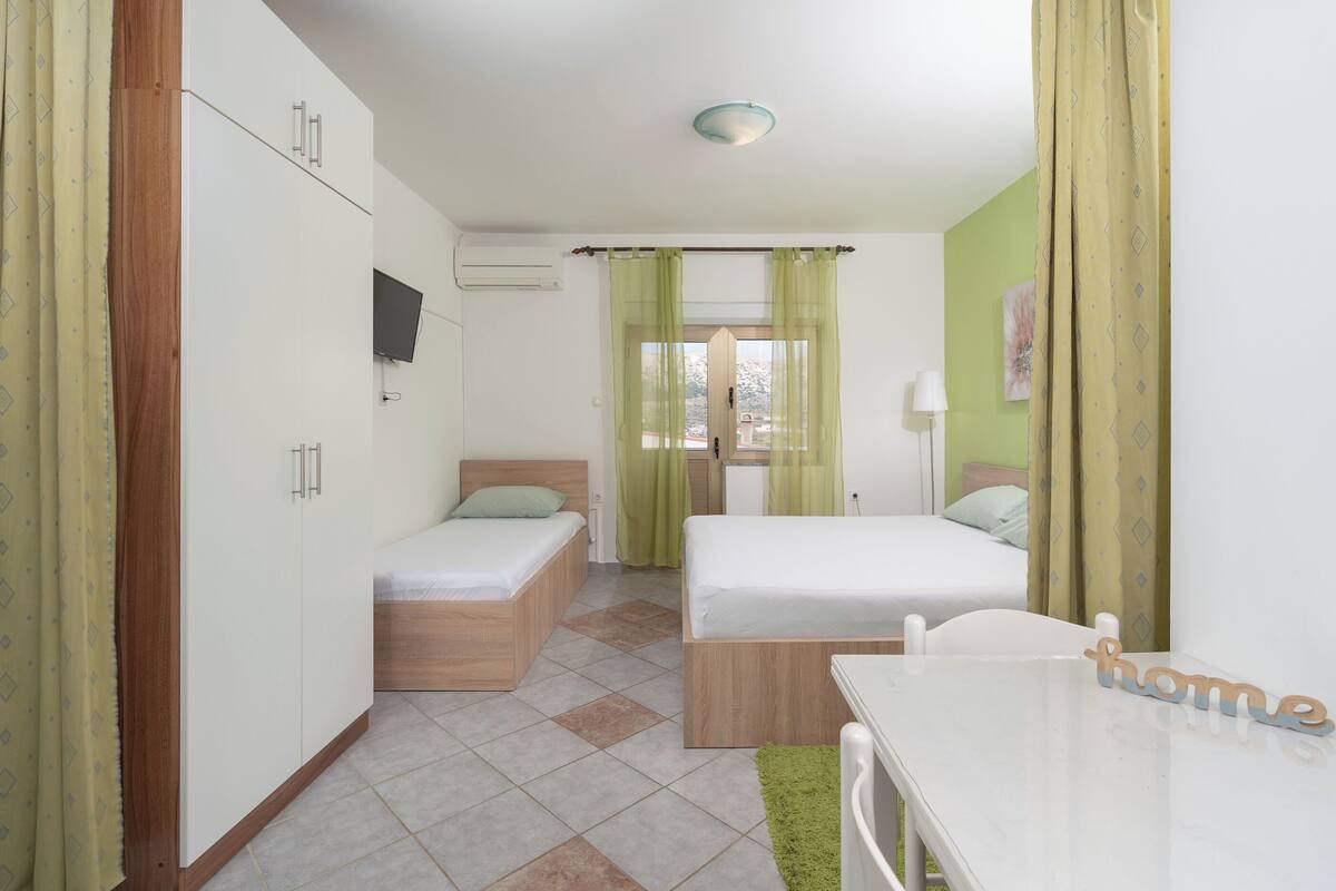 A room with two beds, a desk, a TV, and a window with curtains.