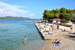 Egy tiszta vizű strand, ahol az emberek úsznak és napoznak, valamint egy sziklás móló.