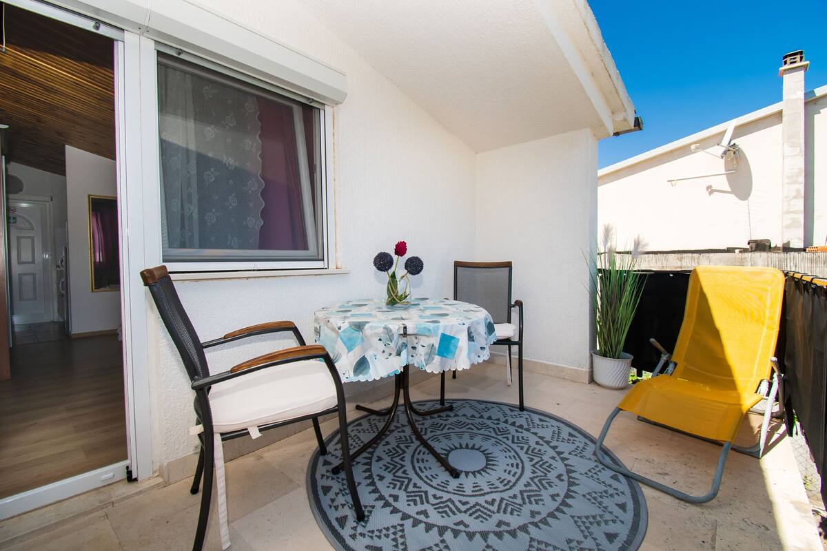 A small patio with a round table, two chairs, a yellow chair, and a patterned rug.