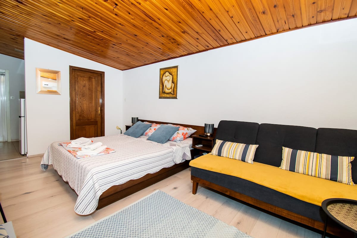 A bedroom with a bed, a sofa, a wooden ceiling, a painting, and a door.