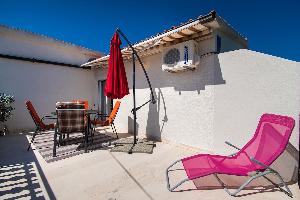 An outdoor patio with a table, chairs, a red umbrella, and a pink chair.