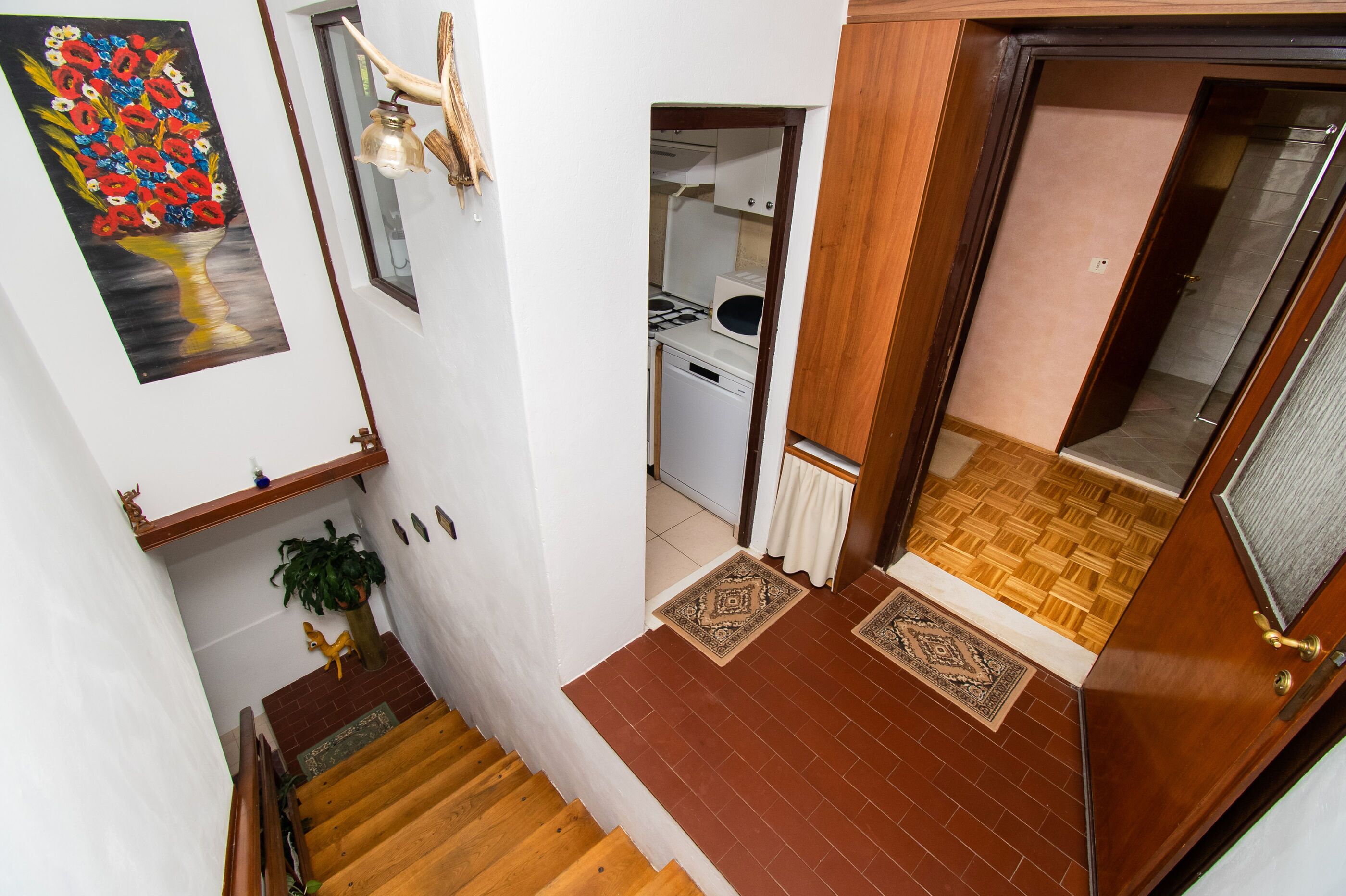 A staircase leading to a room with a wooden door, a small kitchen area, and a decorative painting on the wall.
