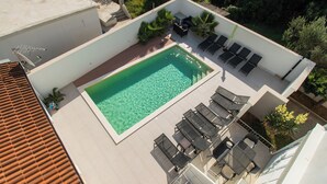An aerial view of a rooftop pool area with a rectangular pool, lounge chairs, and a small table. - Apartment Danijela (Bibinje)