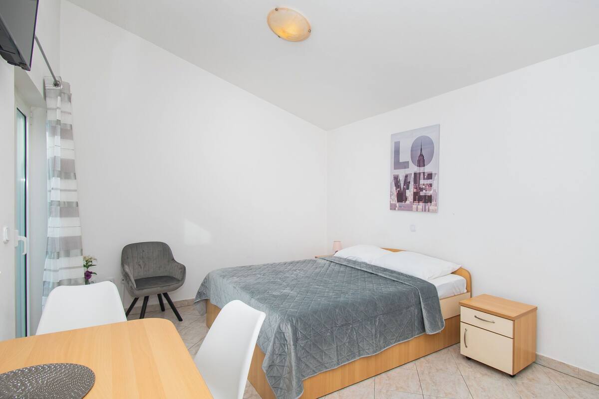 Une chambre à coucher moderne et minimaliste, comprenant un lit, une table de chevet, une chaise et une œuvre d’art accrochée au mur.