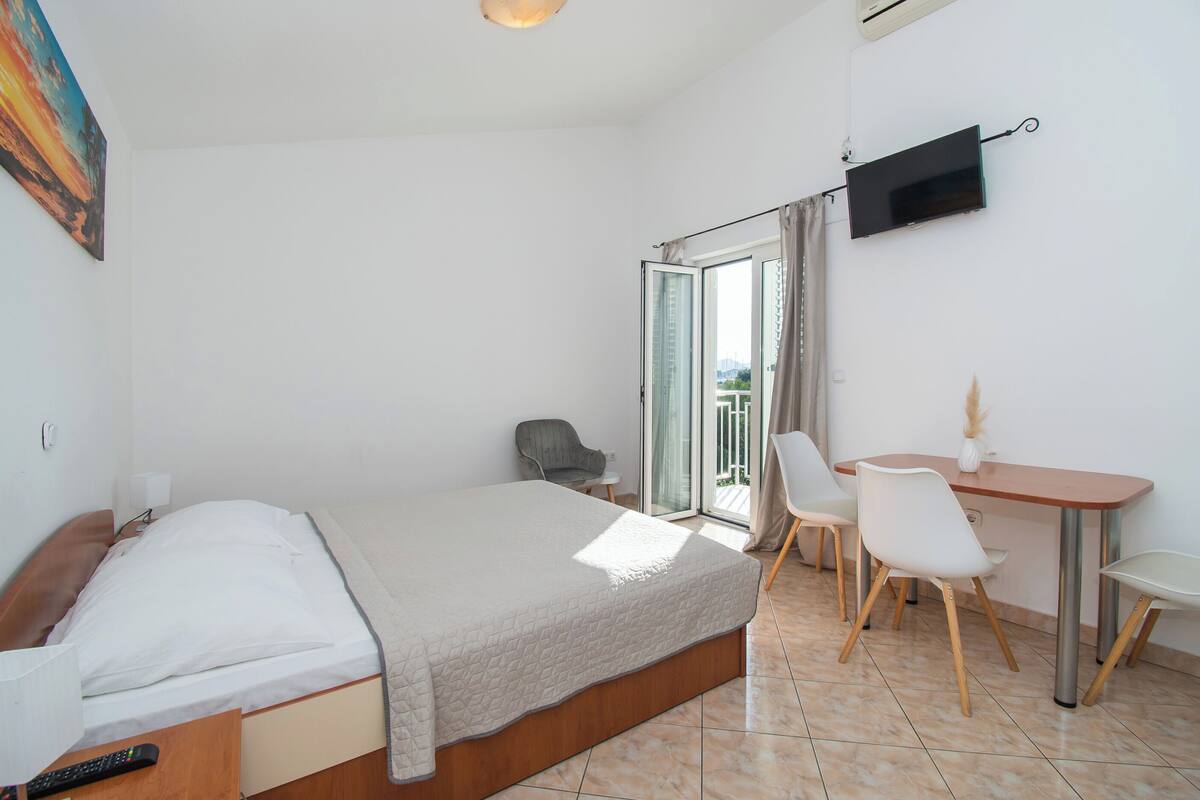Une chambre d’hôtel avec un lit, un bureau avec des chaises, une télévision et une vue sur l’extérieur, visible à travers une porte vitrée.