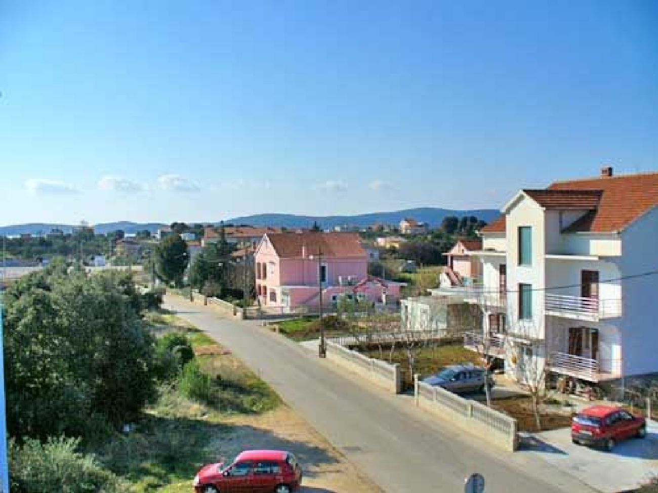 A residential area with houses, a road, and parked cars.