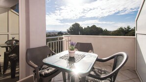 A balcony with a glass table, two chairs, a potted plant, and a view of the sky and distant landscape. - Apartment Danijela (Bibinje)