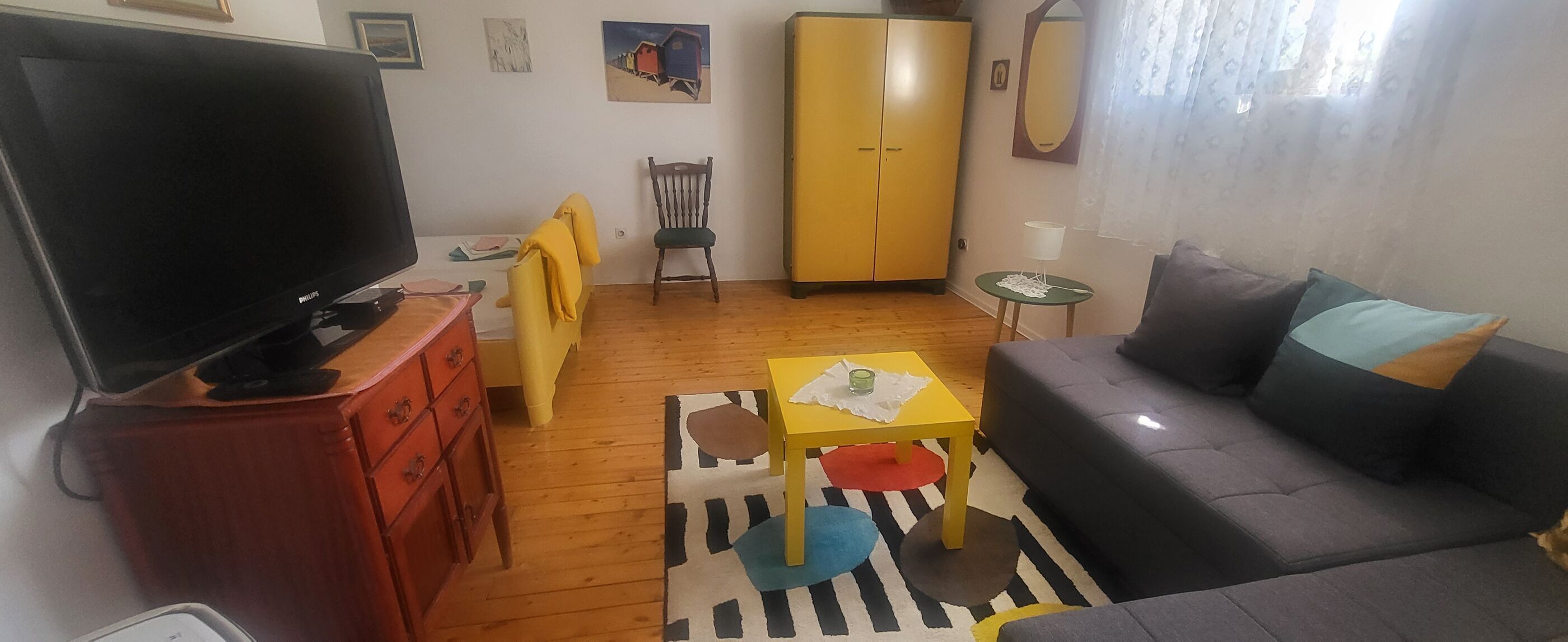 Una sala de estar con televisor, muebles de madera, un mueble amarillo y un sofá gris.