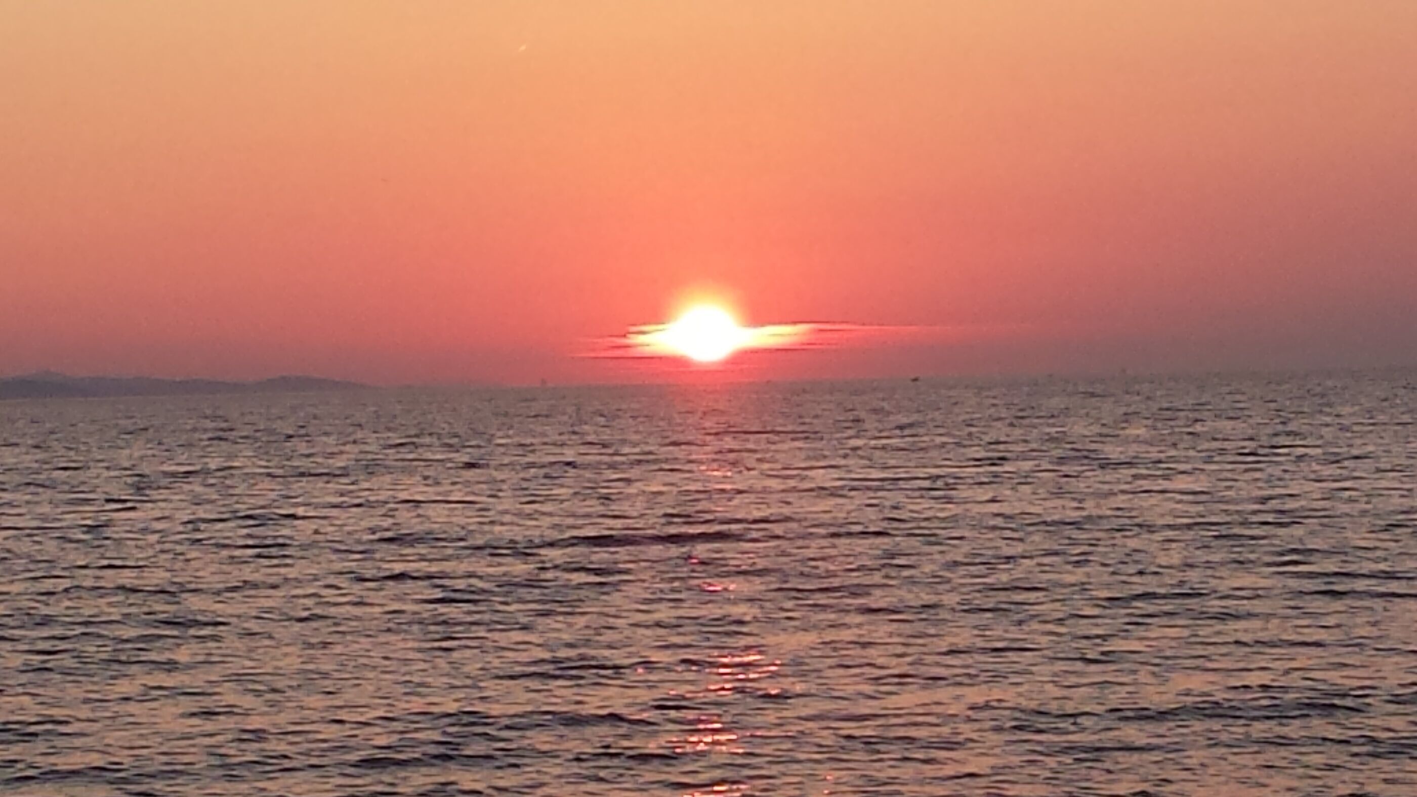 Ein Sonnenuntergang über einem ruhigen Meer mit einer fernen Küste.