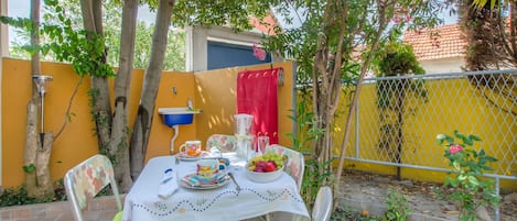 A patio with a table set for two, surrounded by chairs, a yellow wall, and a metal fence.