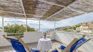 A balcony with a table set for two, two blue chairs, and a view of the sea and hills. - Apartments Amulic (Duce)