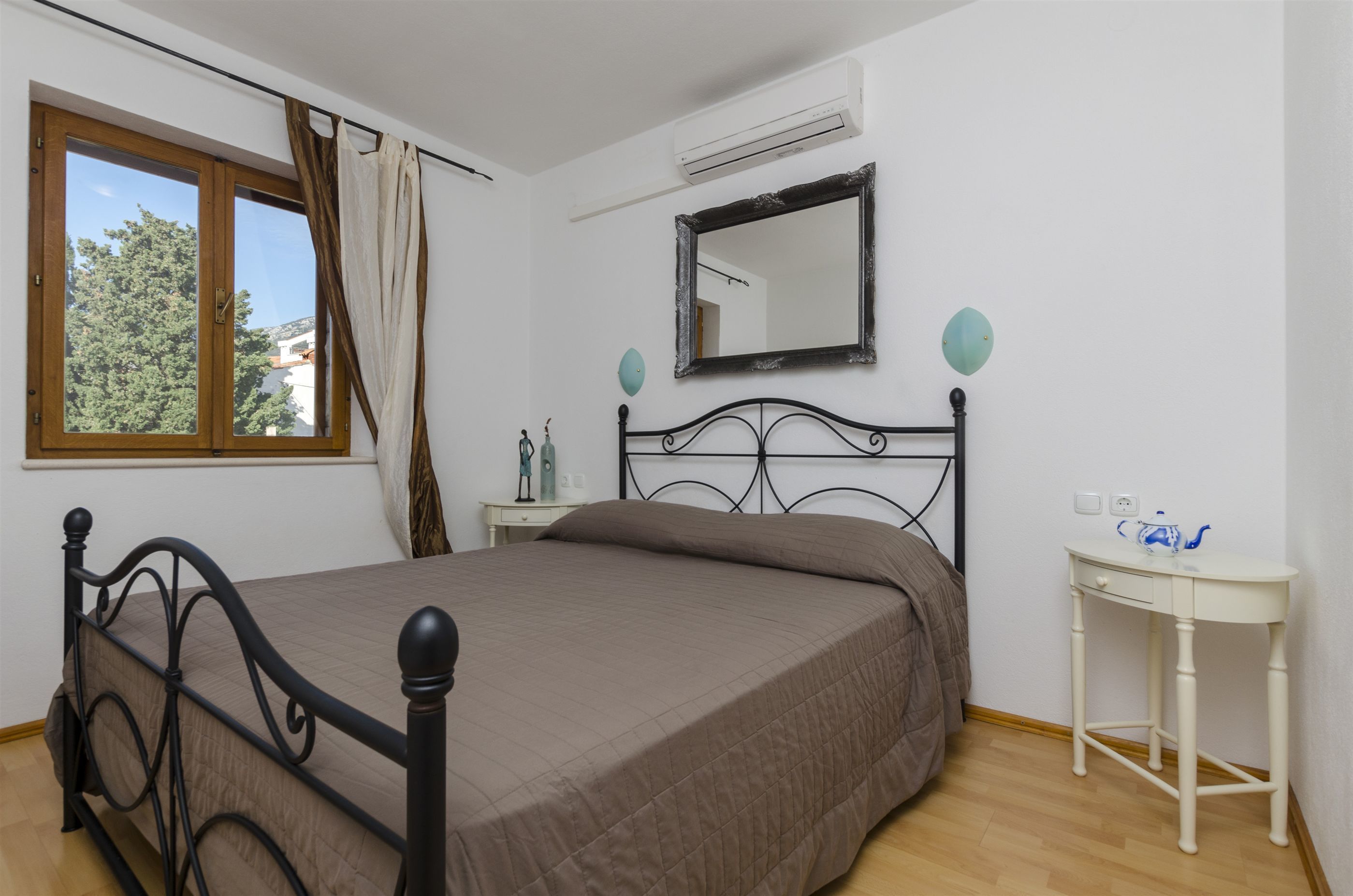 A bedroom with a bed, a bedside table, a mirror, and a window with curtains.