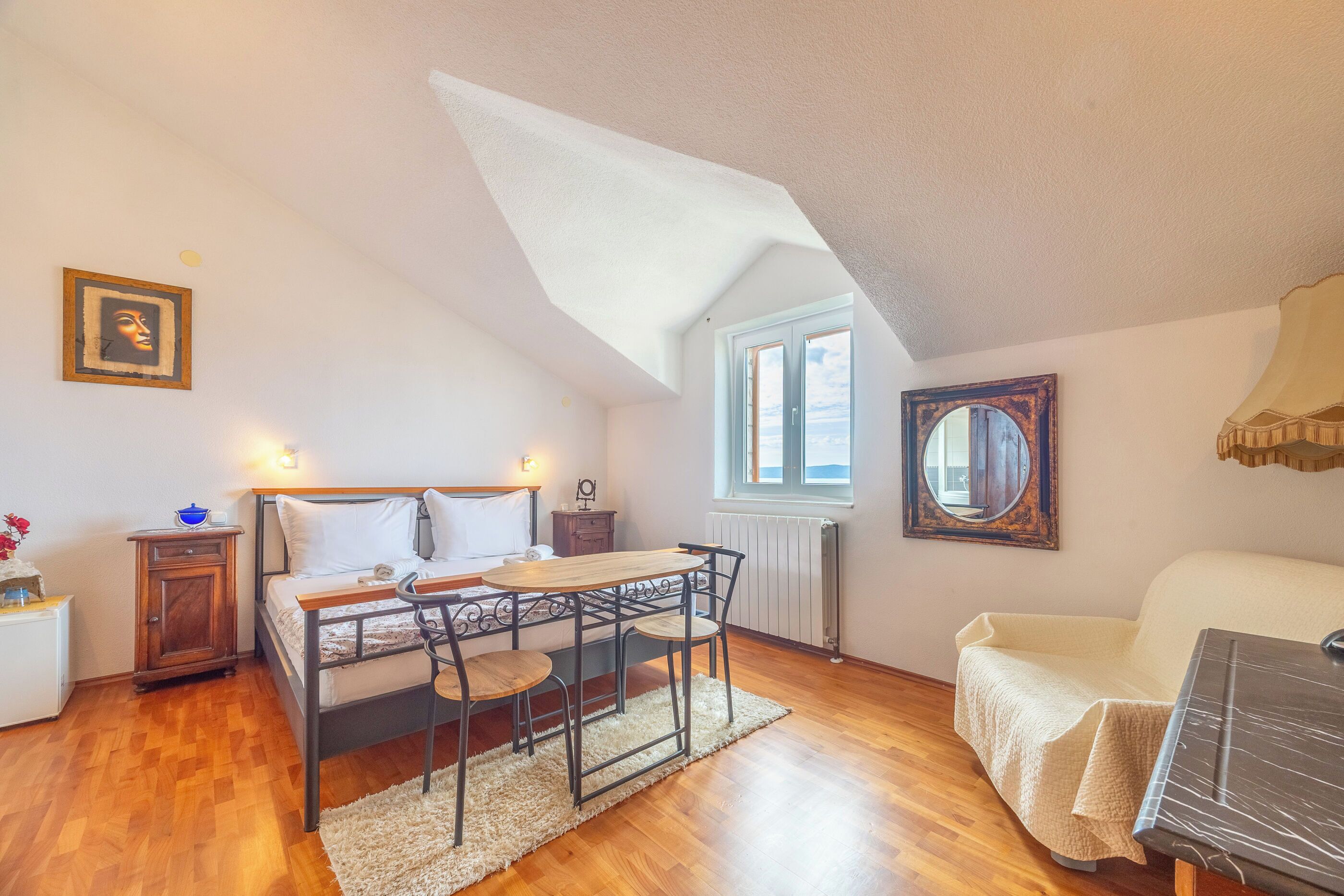 Ein Schlafzimmer mit einem Bett, einem Holztisch mit Stühlen, einem Heizkörper und einem Fenster.