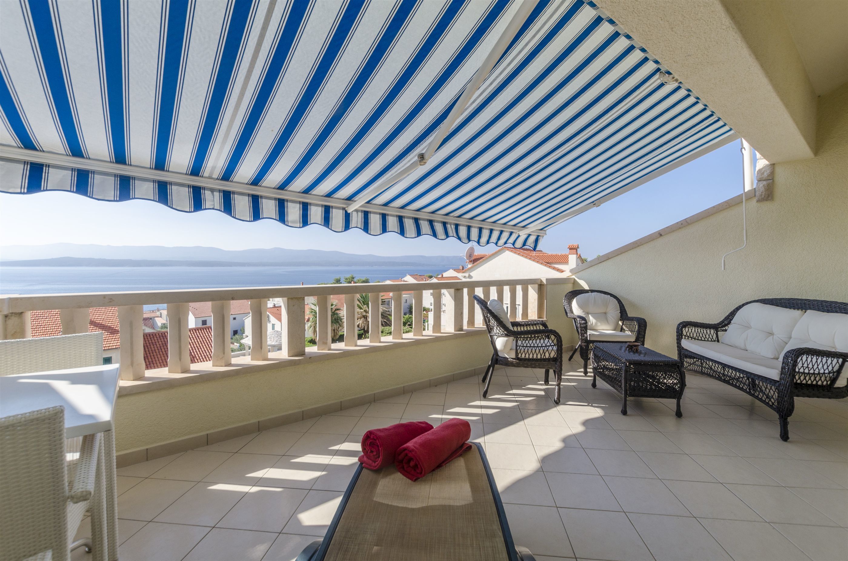 A balcony with a striped awning, wicker furniture, and a view of the sea.