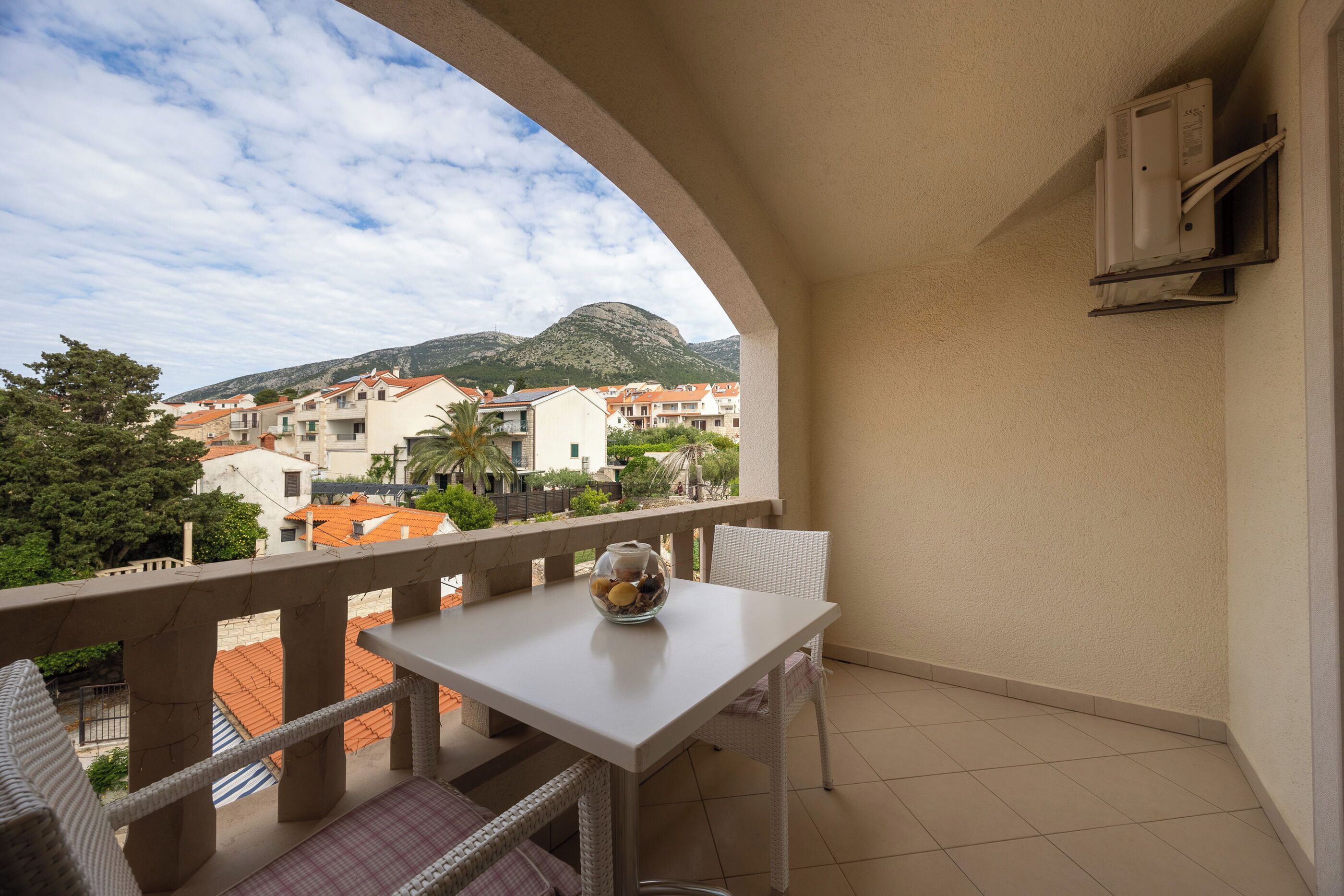 Ein Balkon mit Tisch und Stühlen, der auf ein Wohngebiet mit Häusern und einem Berg blickt.