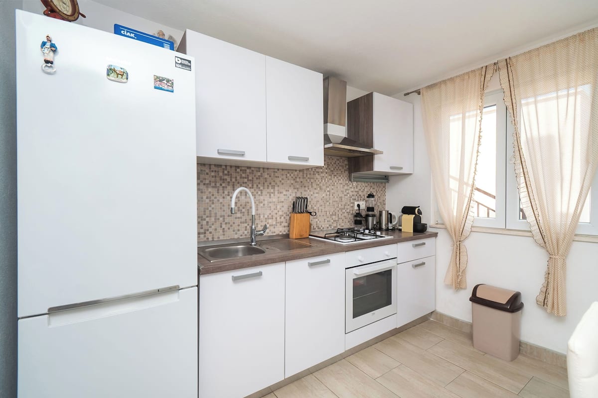 A modern kitchen with white cabinets, a built-in oven, a sink, and a stove.