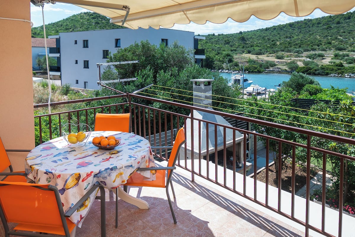 A balcony with a table and chairs, overlooking a body of water and buildings.
