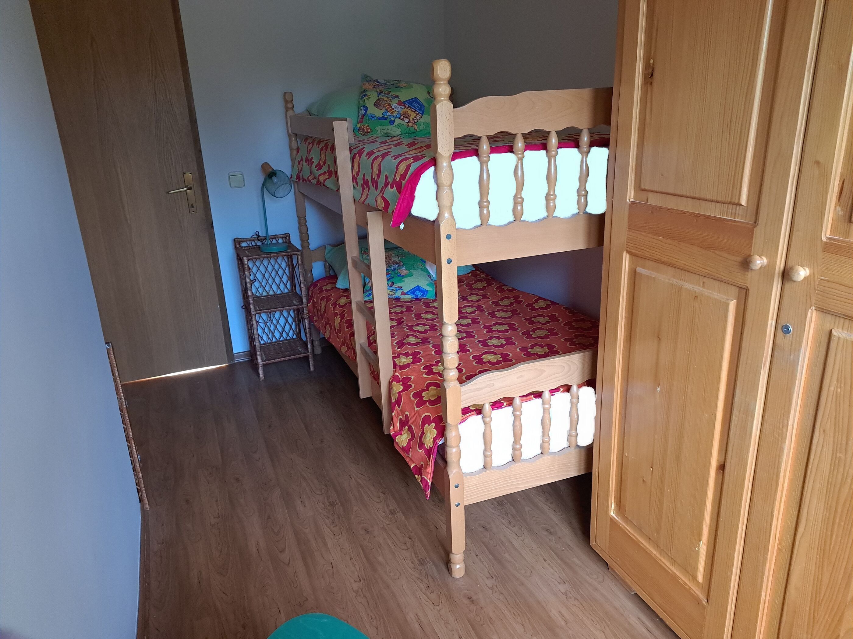 A room with two bunk beds, a wooden wardrobe, and a small wicker shelf.