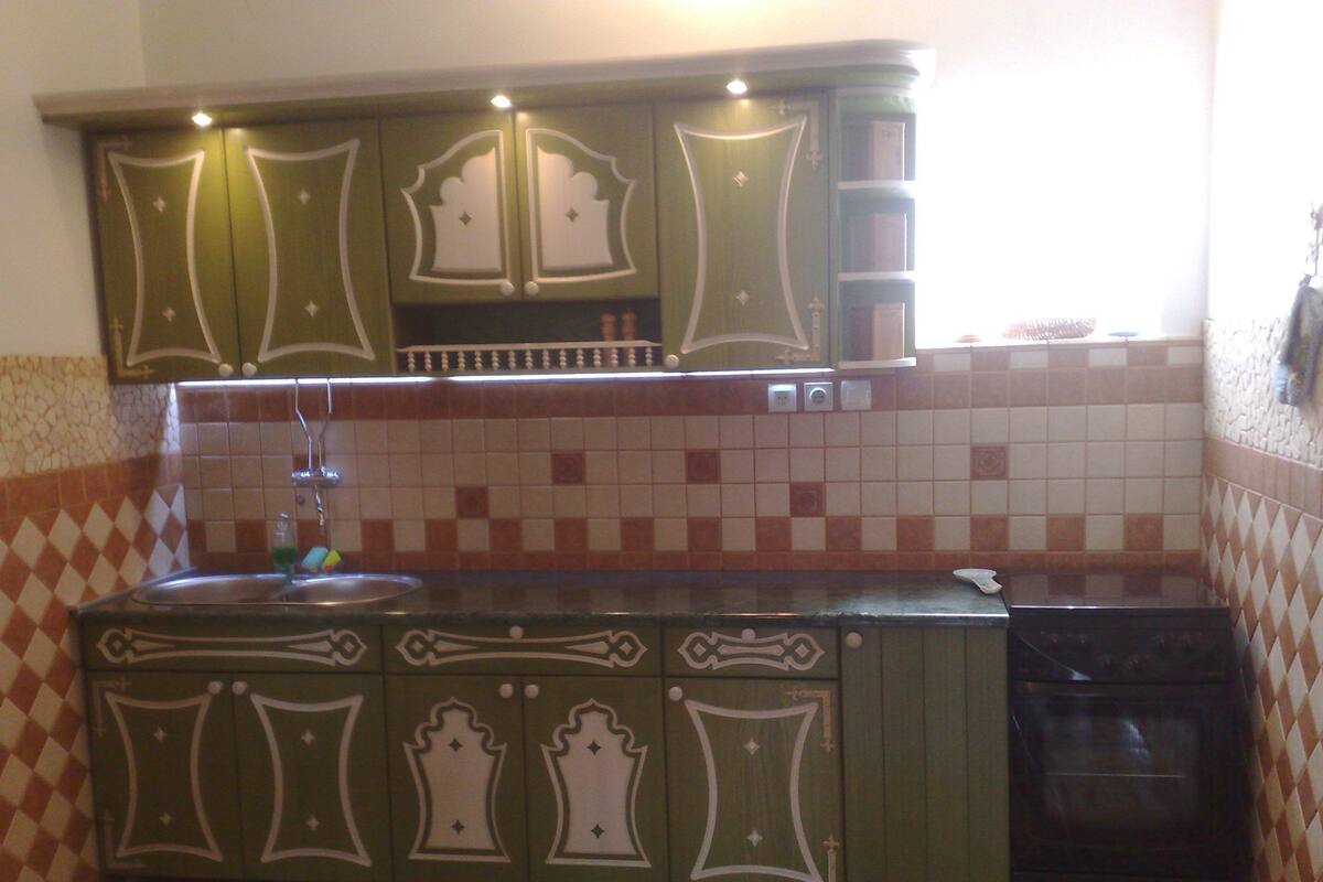 Una cocina con gabinetes verdes, salpicadero de azulejos y lavavajillas.