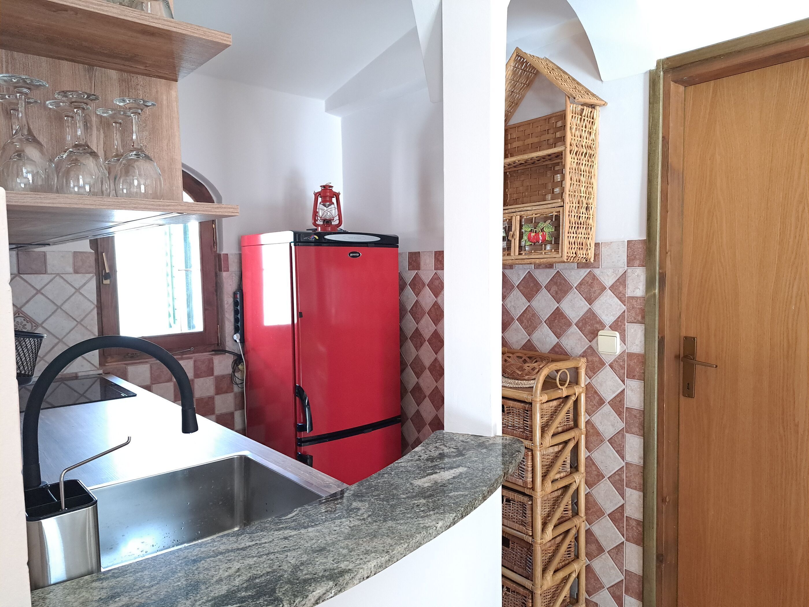 A compact kitchen with a red refrigerator, a sink, and a window.