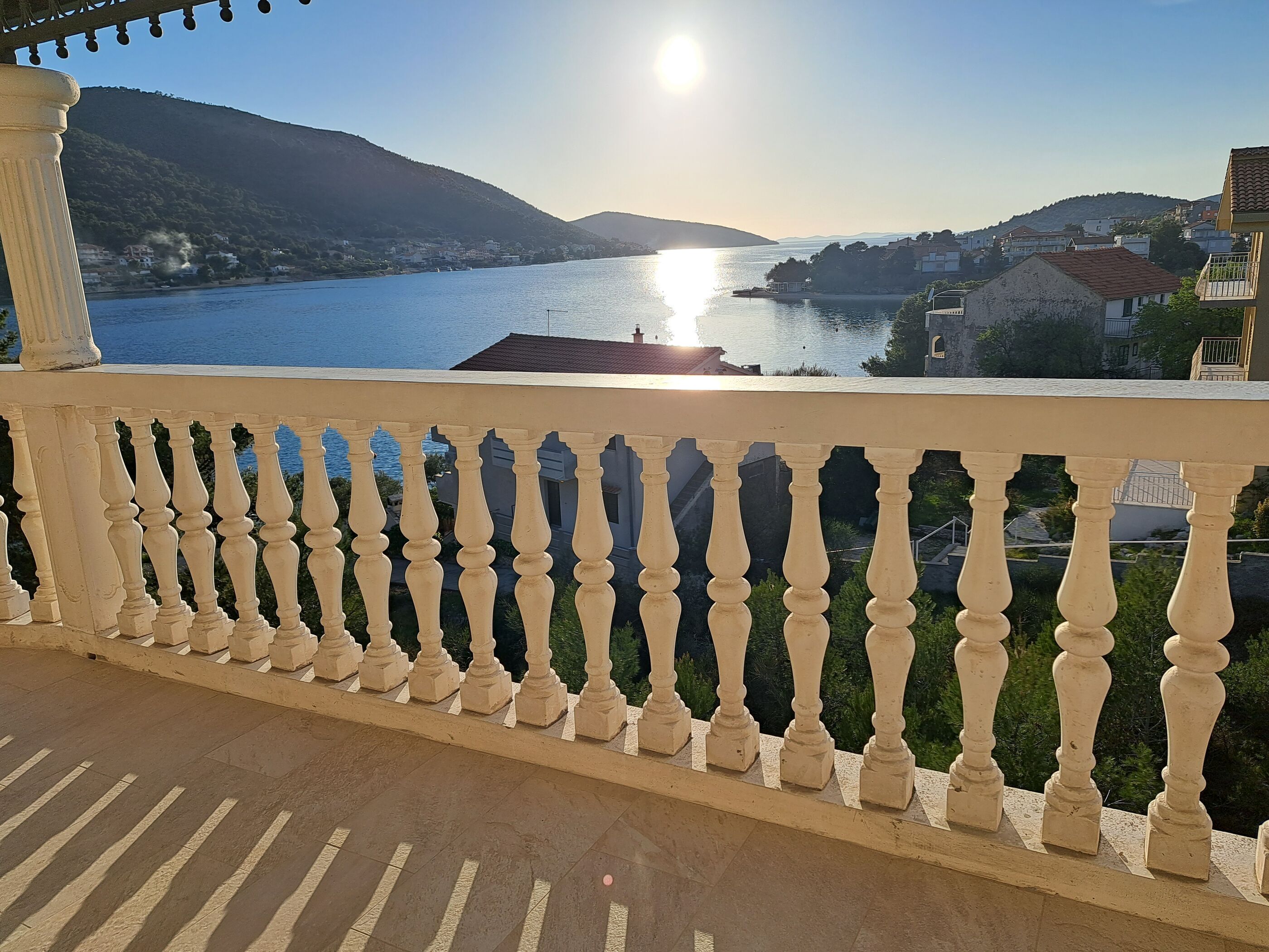 Un balcon doté d’une balustrade, offrant une vue sur une étendue d’eau et un paysage vallonné.