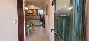 A narrow hallway leading to a kitchen with a stone archway, a dining table with chairs, and a green door. - Apartments Nediljka (Grebastica)