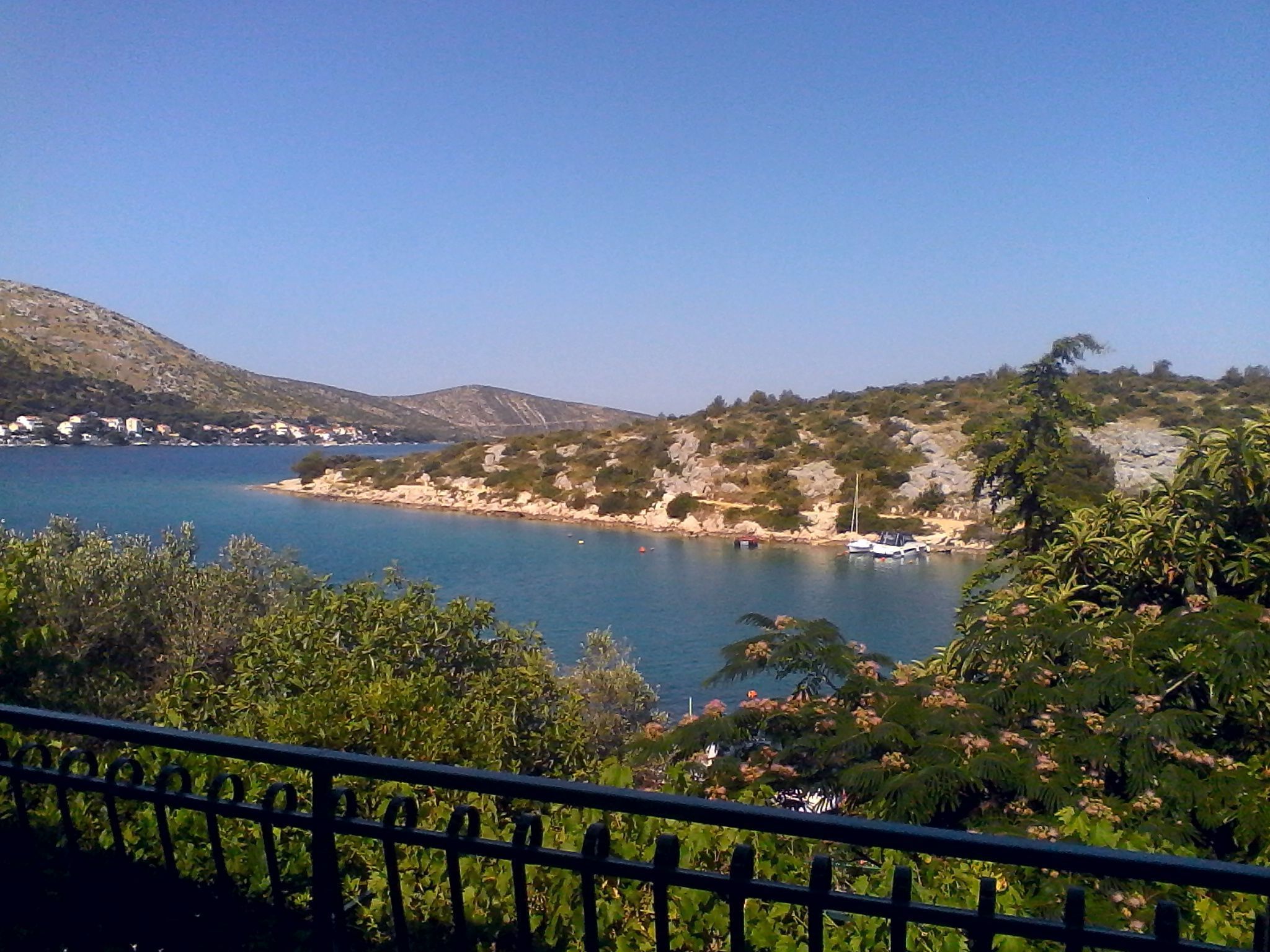 A coastal landscape with a clear view of the sea, a rocky shoreline, and a few boats.