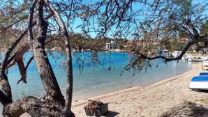 Una playa con mar azul cristalino, barcos y un árbol con una cuerda y un balde en la arena.