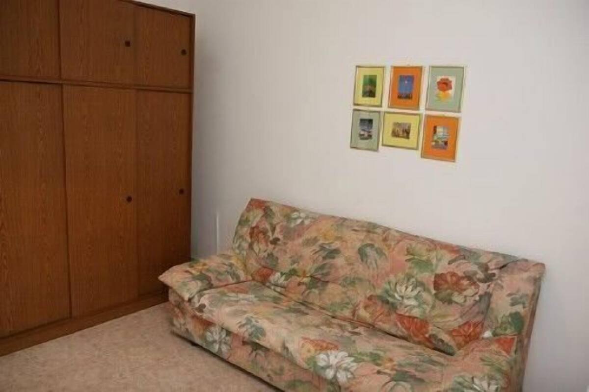 Una habitación con un sofá estampado con motivos florales, un armario de madera y cuatro cuadros en la pared.