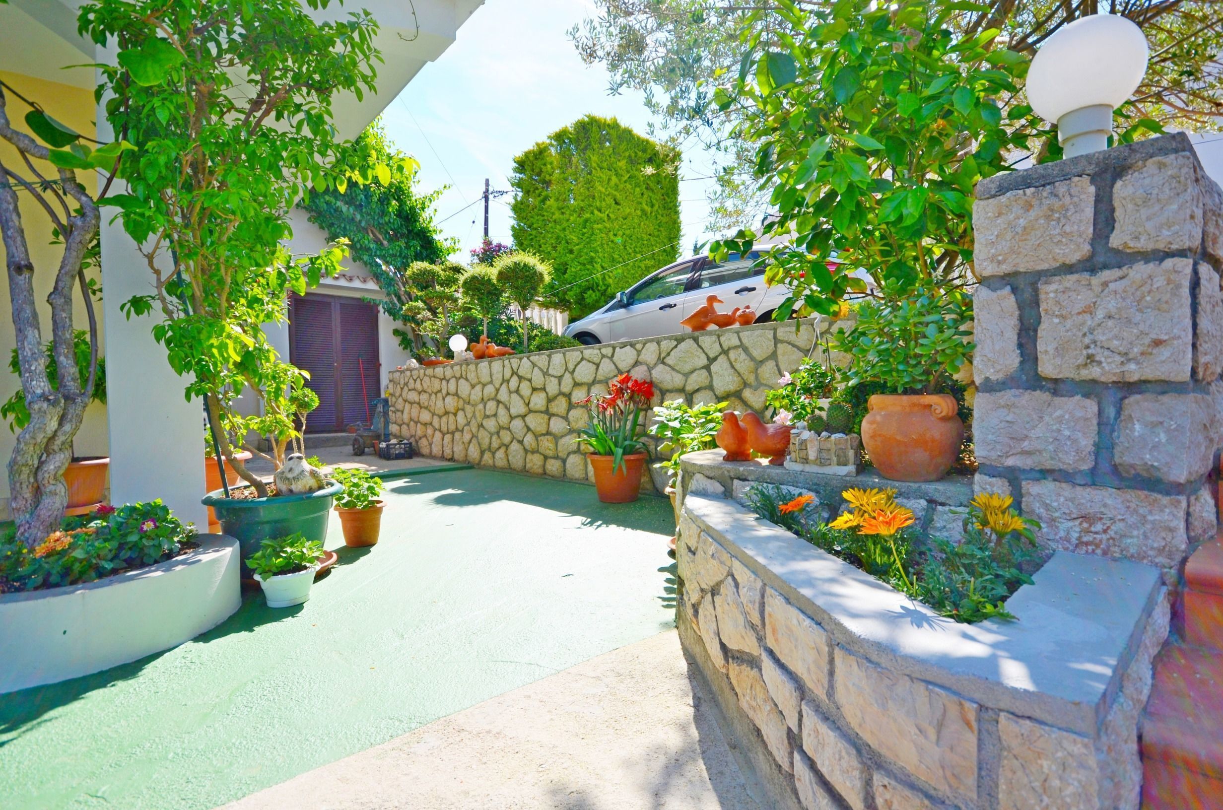 A courtyard with a stone wall, potted plants, and a car parked in the background.