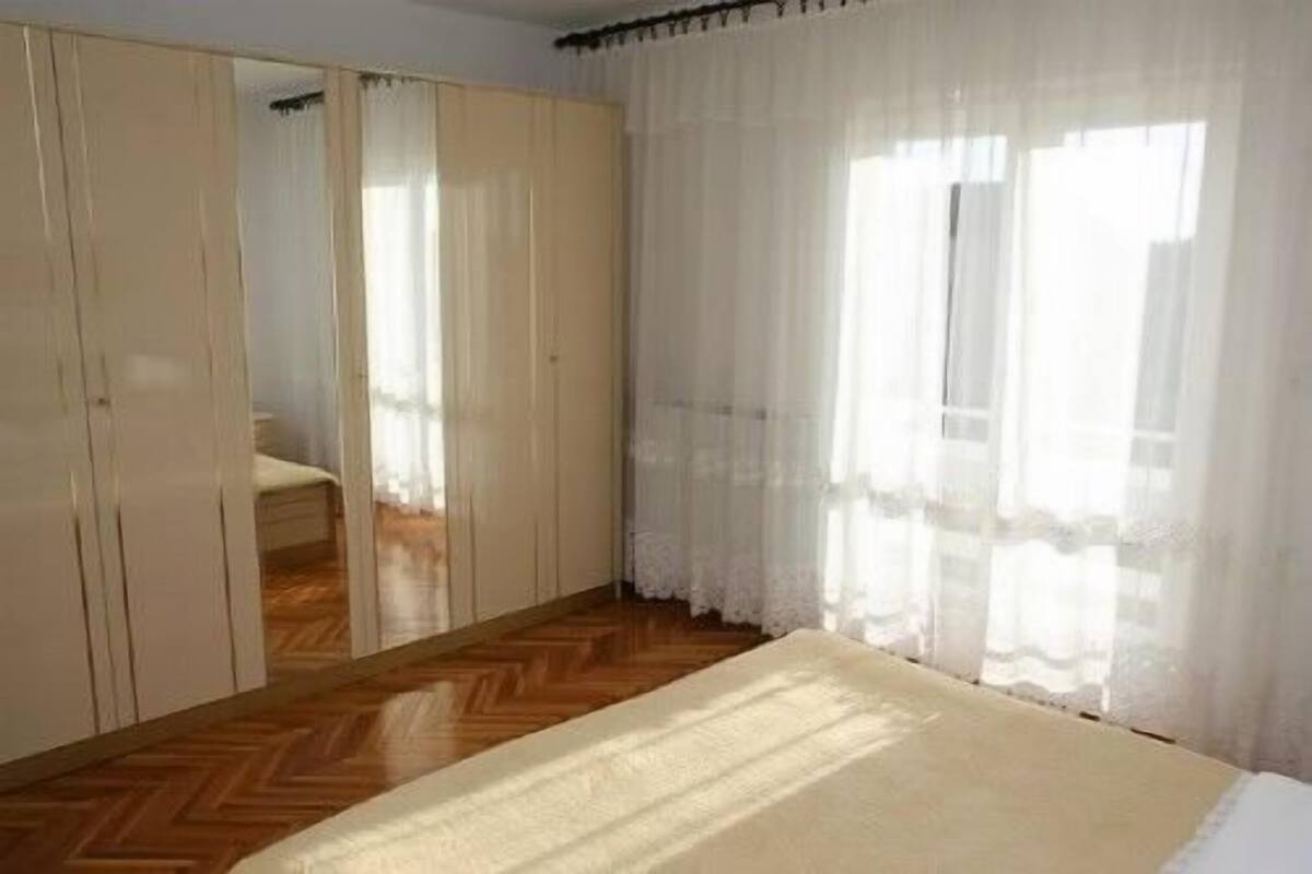 Un dormitorio con cama, suelo de madera, armario y cortinas de gasa.