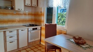 Et kompakt køkken med gaskomfur, ovn og et spiseområde med bord og stol.